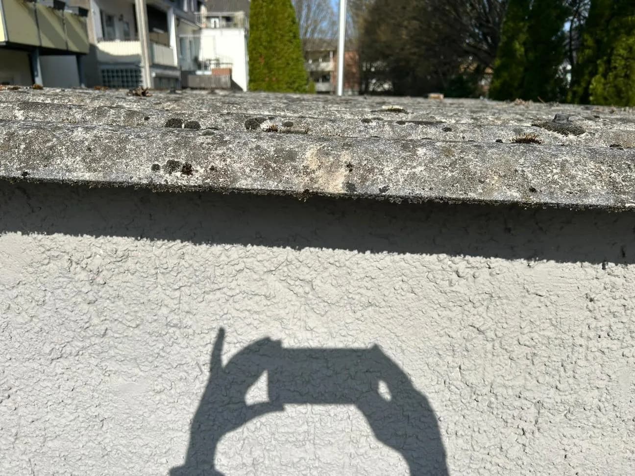 Asbestzement-Platten am Dachrand über verputzter Wand